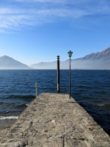 Molo in pietra ad Ascona sul Lago Maggiore, con un lampione e le montagne sullo sfondo
