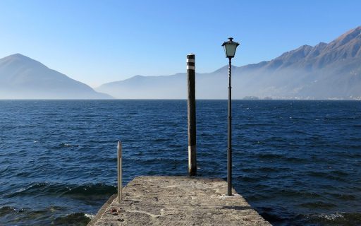 Molo in pietra ad Ascona sul Lago Maggiore, con un lampione e le montagne sullo sfondo